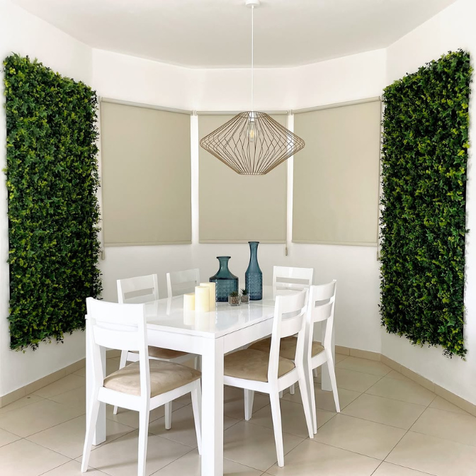 Indoor dining room with artificial green wall panels 40x40 as vertical greenery decor next to a white dining table and chairs