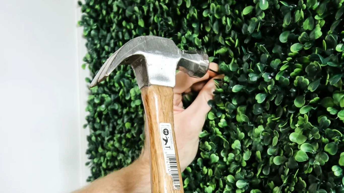 DIY installation of artificial green wall panels using hammer and nail, showing simple method for living wall setup