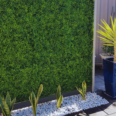Texto alt (accesible + keywords long-tail):
Artificial Boxwood Hedge Wall installed outdoors with white decorative stones and potted plants, a low-maintenance greenery solution by Green Warehouse.