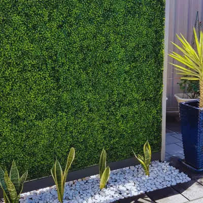 Artificial Boxwood Hedge Wall installedoutdoors with white decorative stones and potted plants, a low-maintenance greenery solution by Green Warehouse.