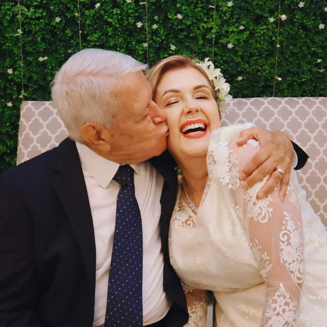 Bride smiling with family in front of artificial green wall backdrop with white flower accents creating a timeless wedding photo setting