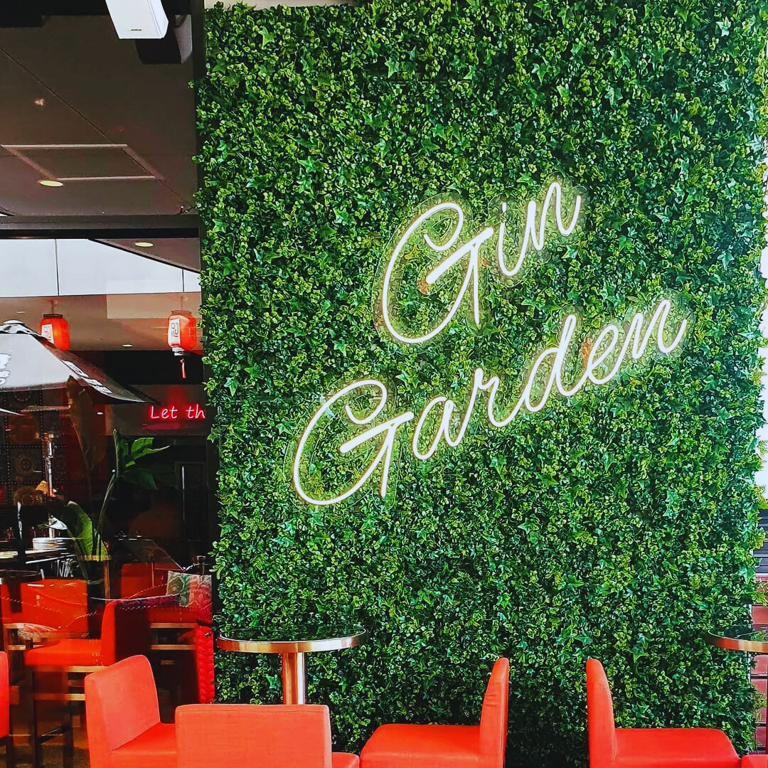 Restaurant interior with artificial green wall and neon sign creating stylish greenery decor with red chairs and tables