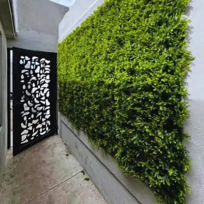 Japanese Fern artificial hedge wall with vibrant lime and deep green leaves installed on an outdoor concrete wall.