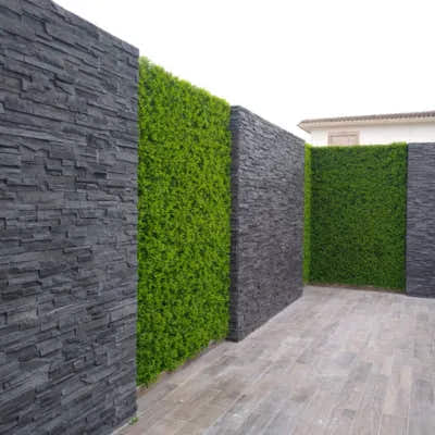 Japanese Fern artificial hedge panels installed between dark stone walls, creating a modern outdoor patio design