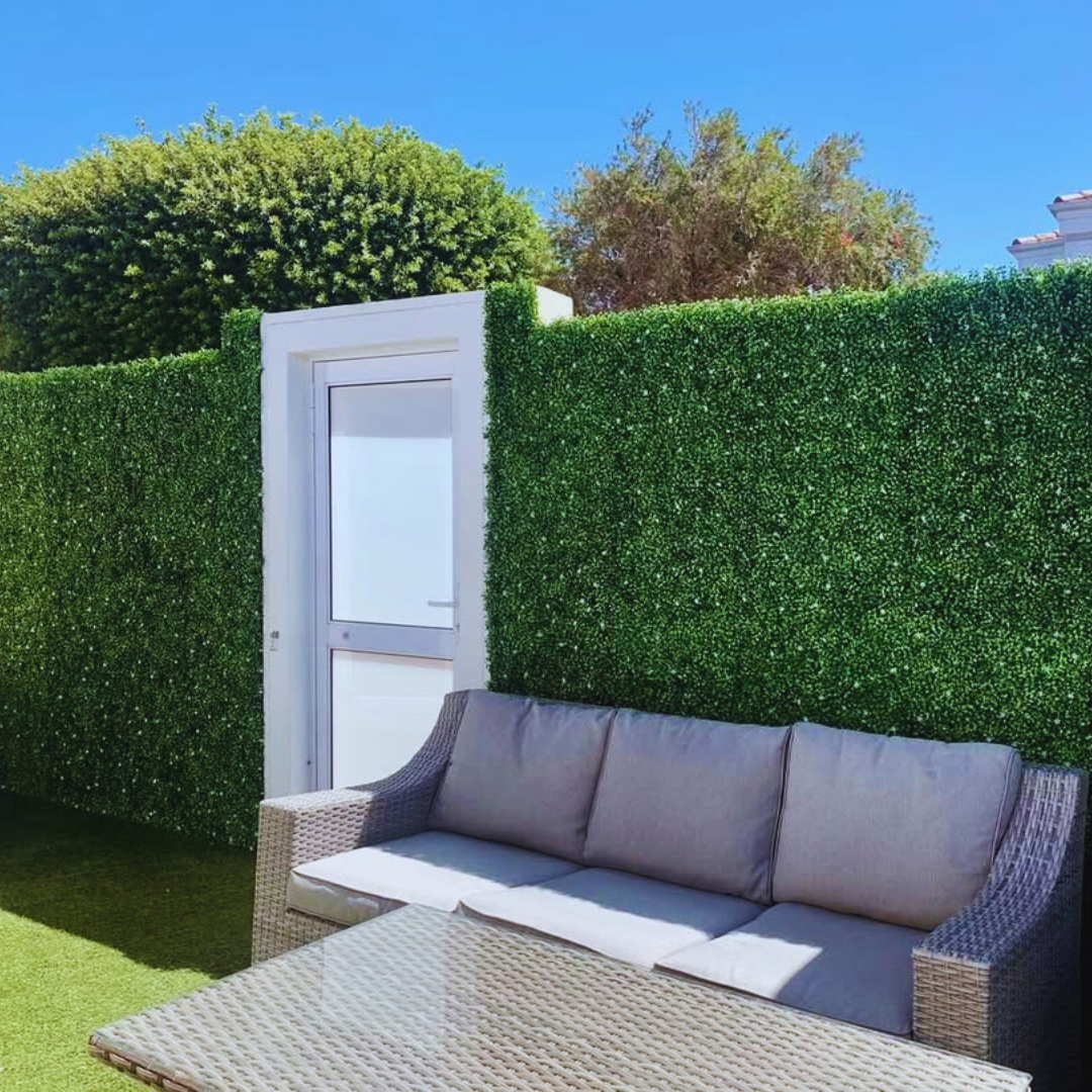 Modern outdoor patio with artificial green wall panels and wicker sofa set creating UV-protected privacy hedge