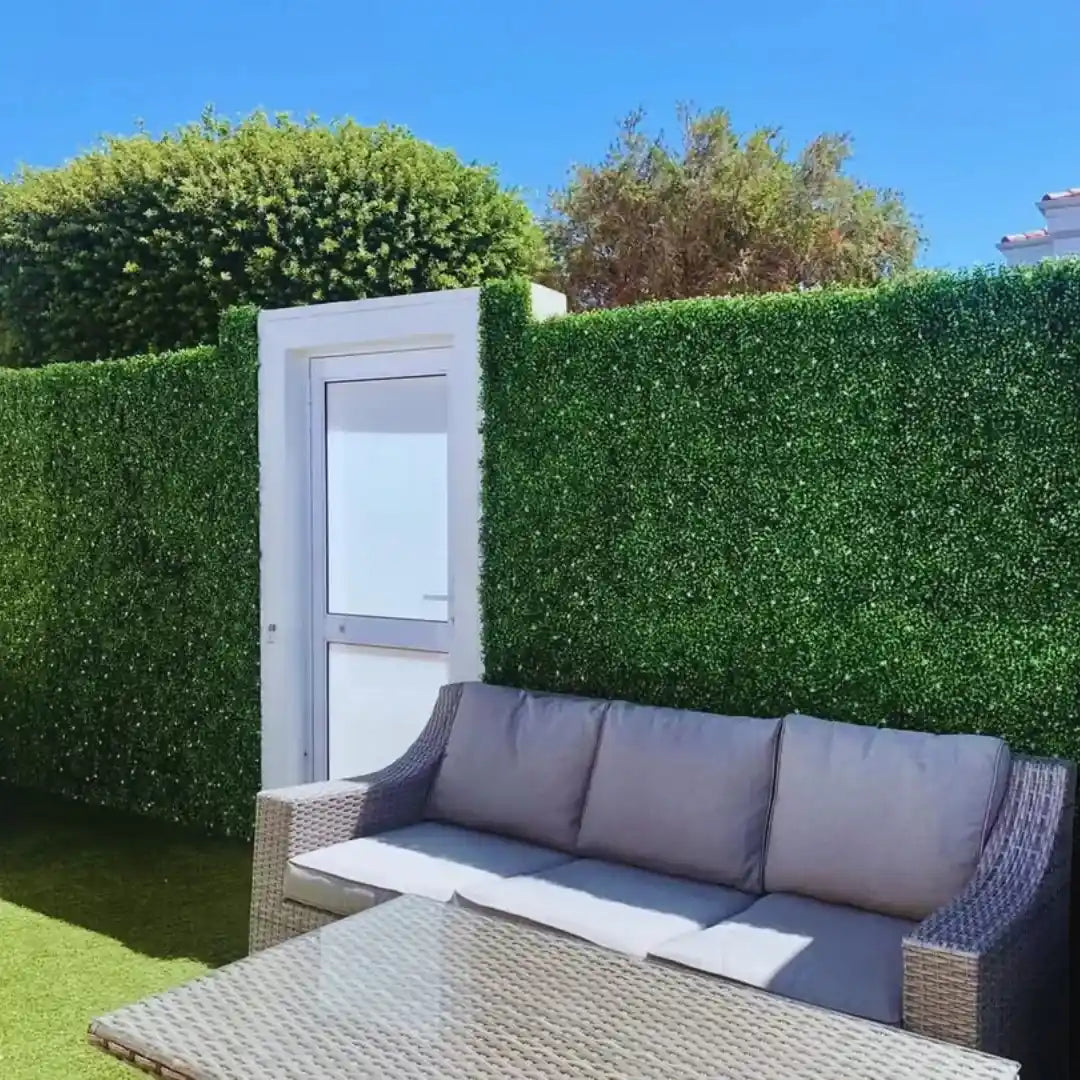 Modern outdoor patio with artificial green wall panels and wicker sofa set creating UV-protected privacy hedge